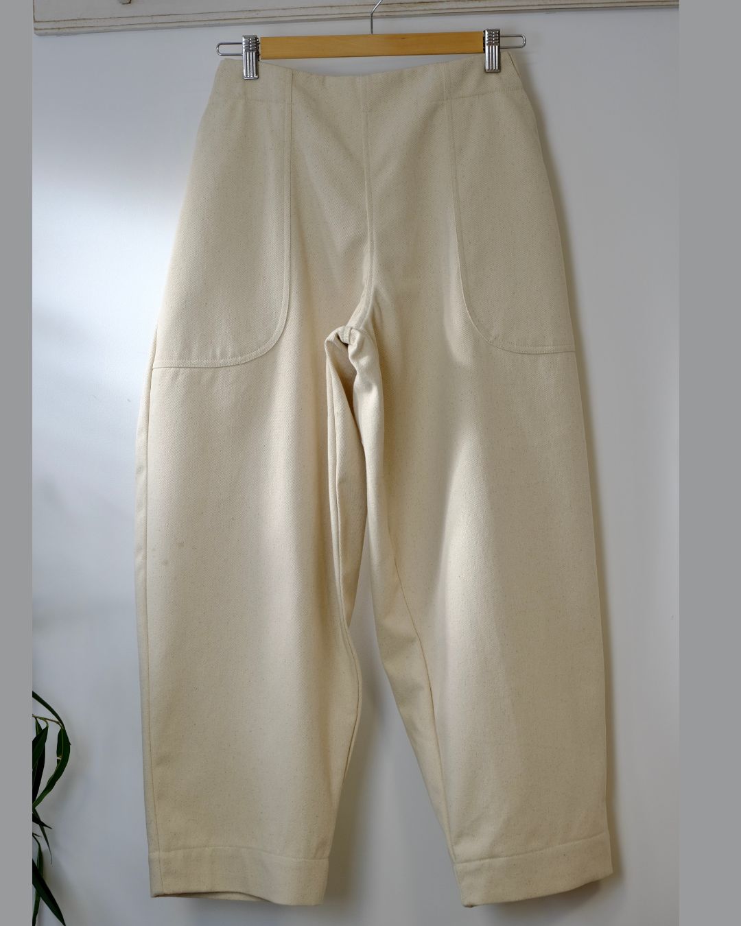 Beige pants hanging on a wooden hanger against a white wall