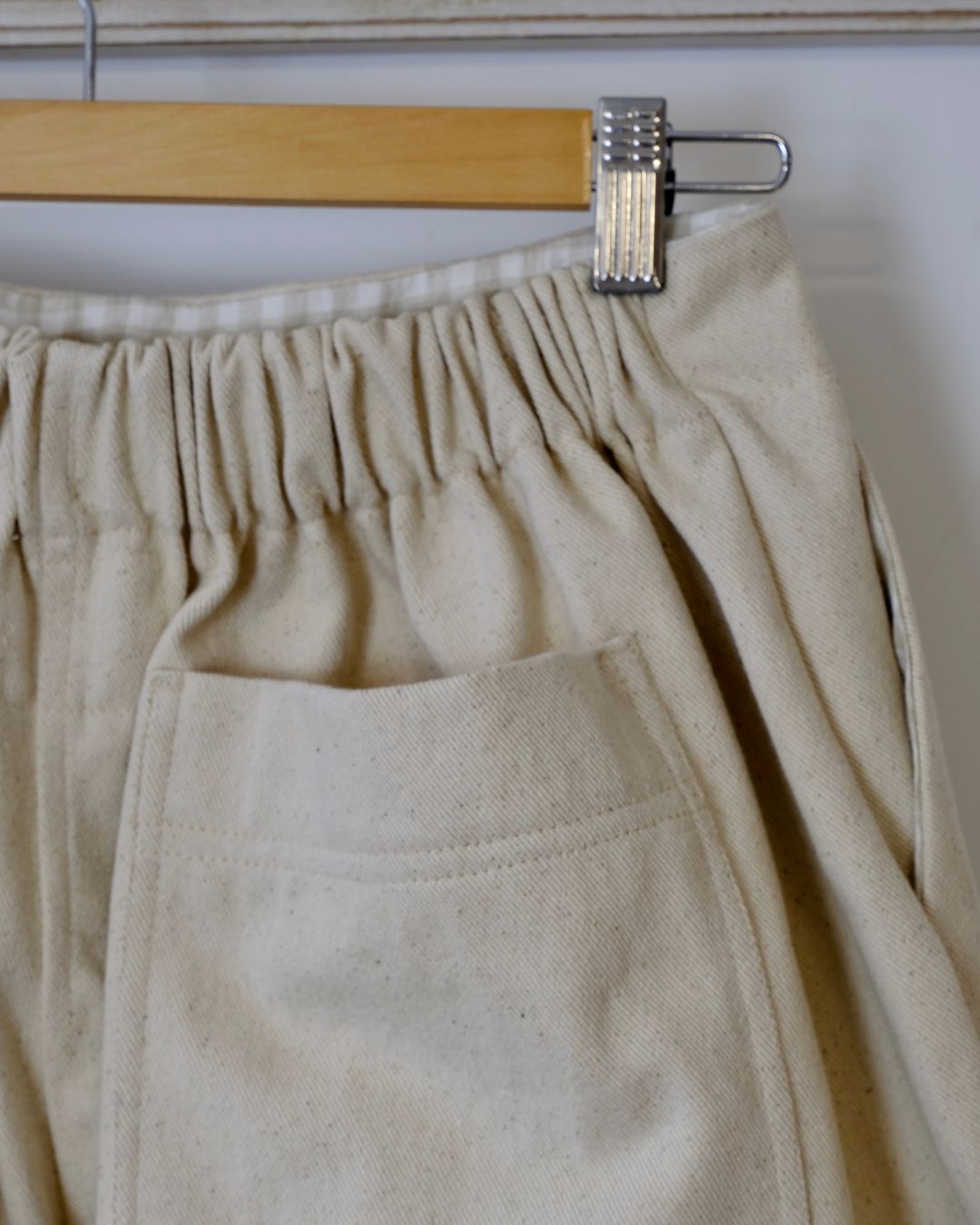 Beige pants hanging on a wooden hanger against a white background