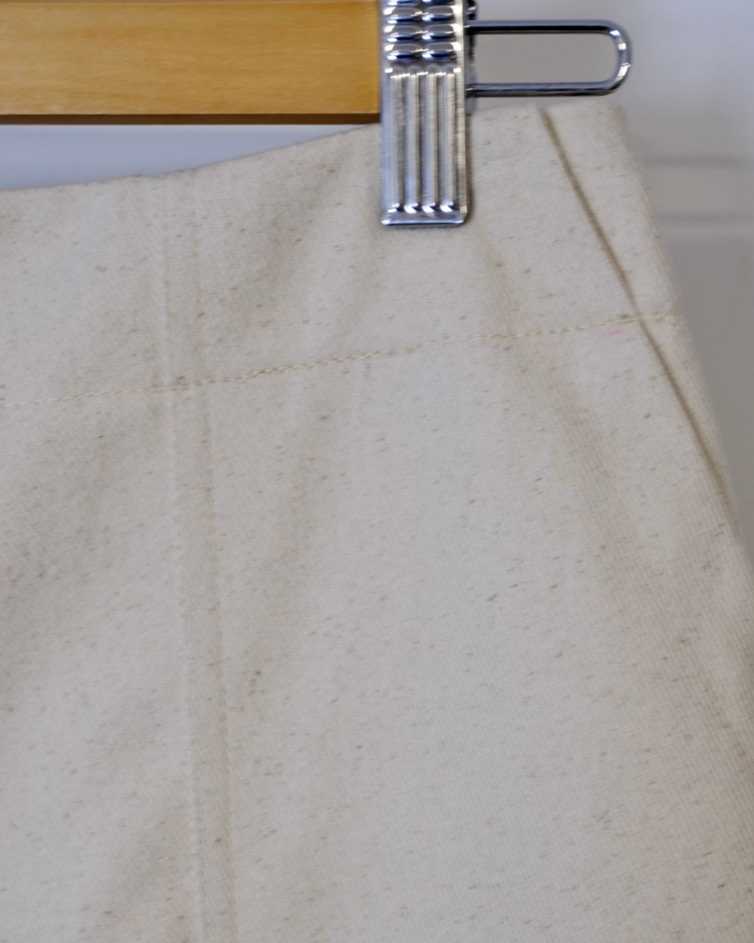 Close-up of beige fabric with a metal clip on a wooden hanger.