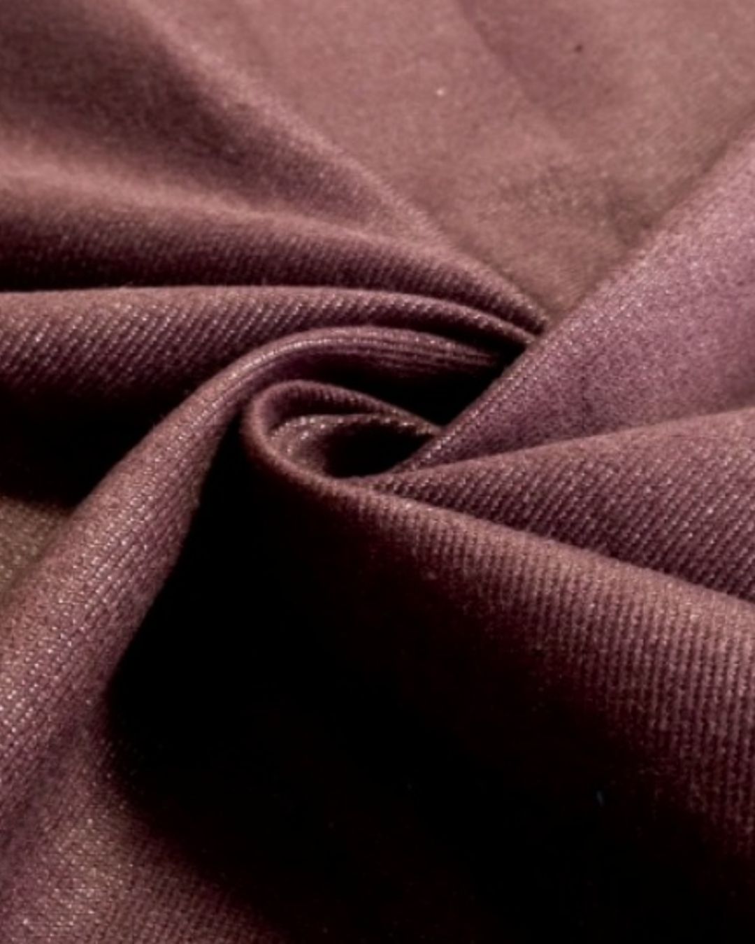 A close-up of draped fabric in a deep plum or eggplant purple color, showing the texture and weave.