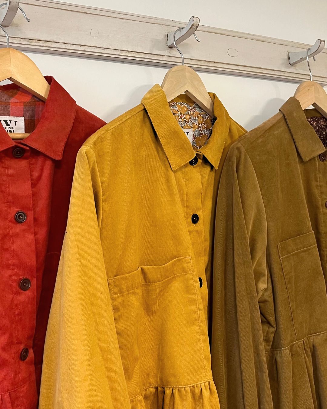 Three corduroy shirts in red, yellow, and brown hanging on a rack.