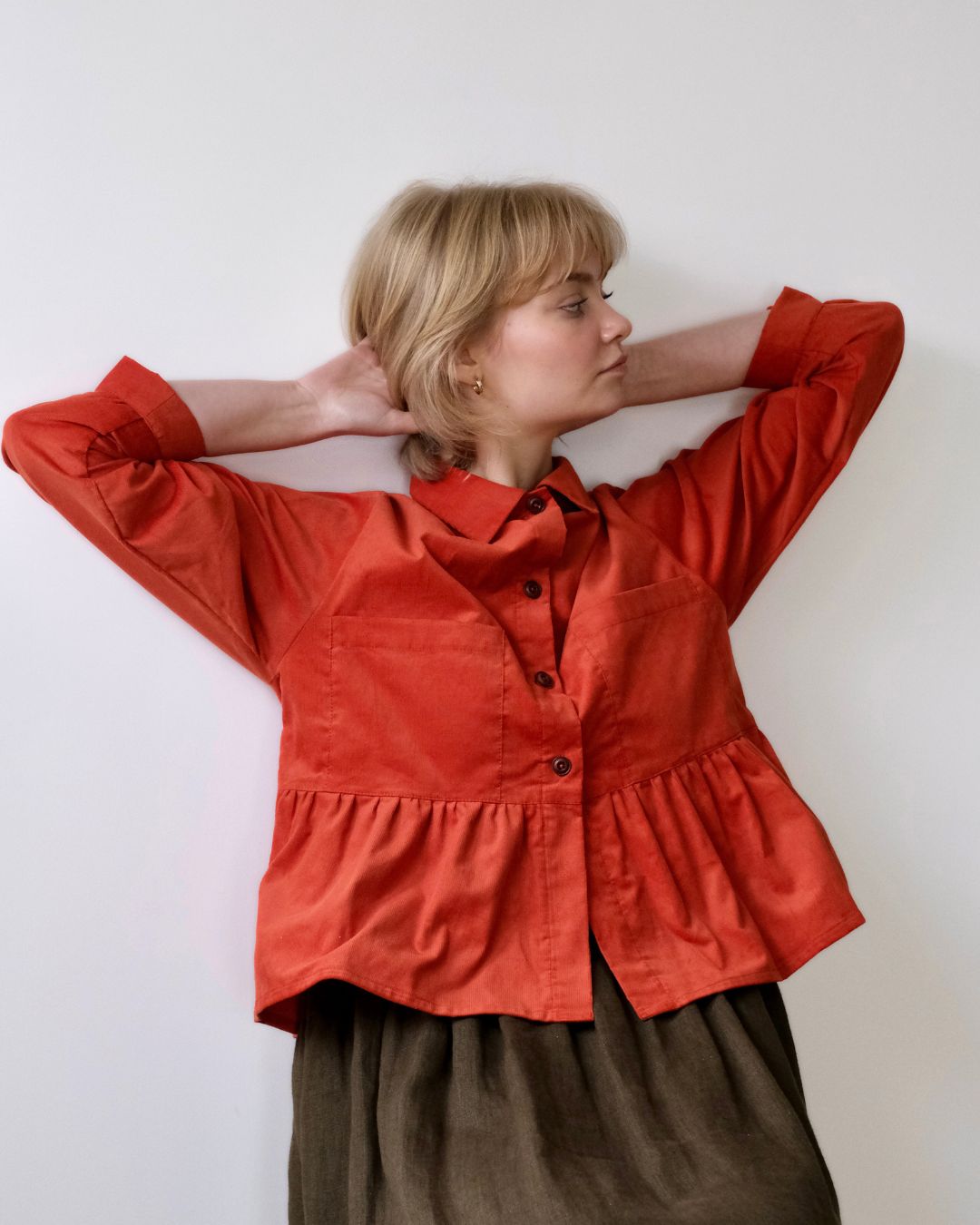 A person modeling a red needlecord shirt with patch pockets, a neat collar with a contrast floral print, and bracelet length sleeves finished with a cuff.