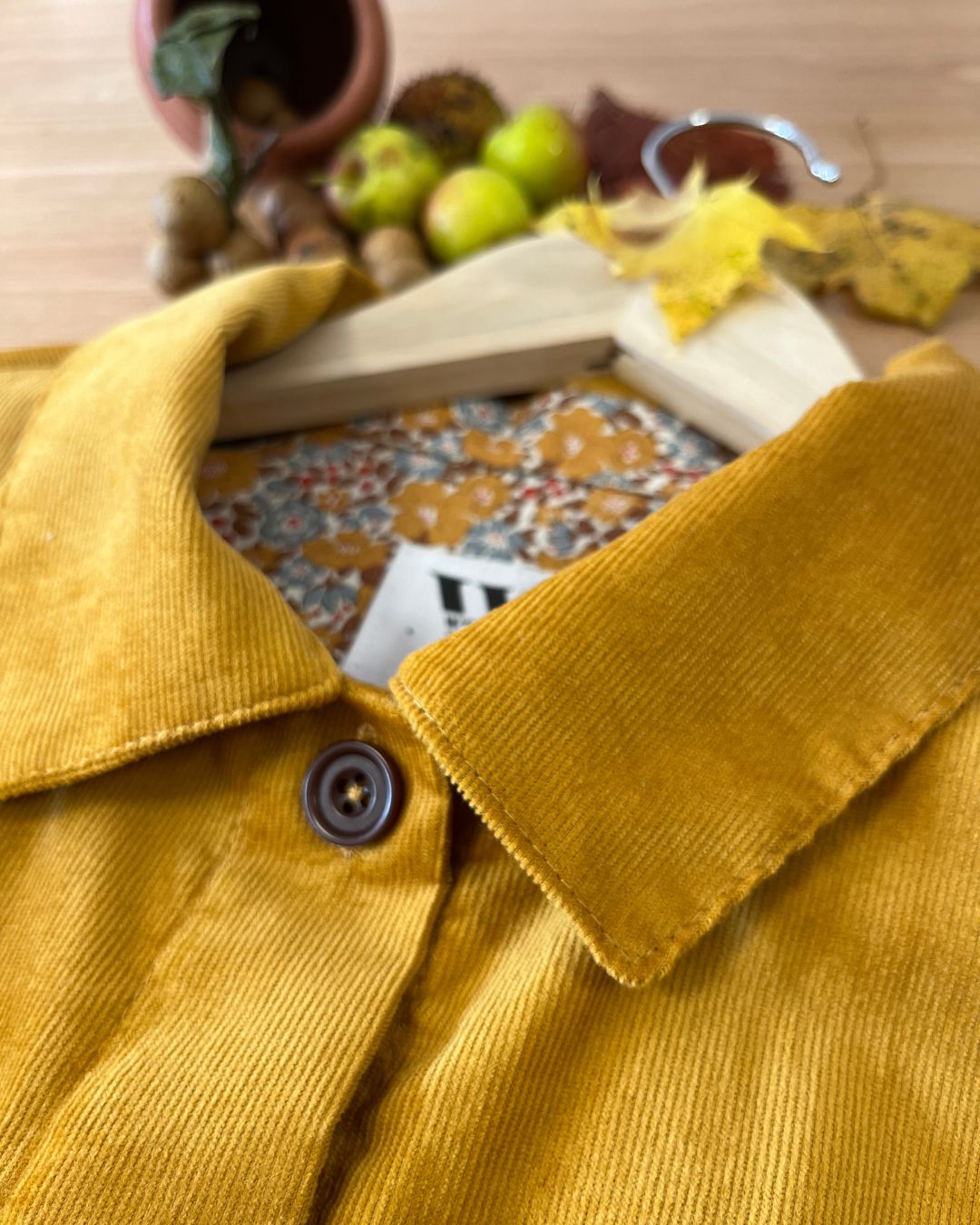 Close-up of an ochre yellow corduroy shirt collar with a patterned fabric and autumnal elements in the background.