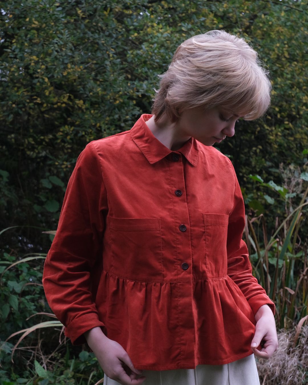 Person wearing a red jacket standing in a natural setting with greenery.