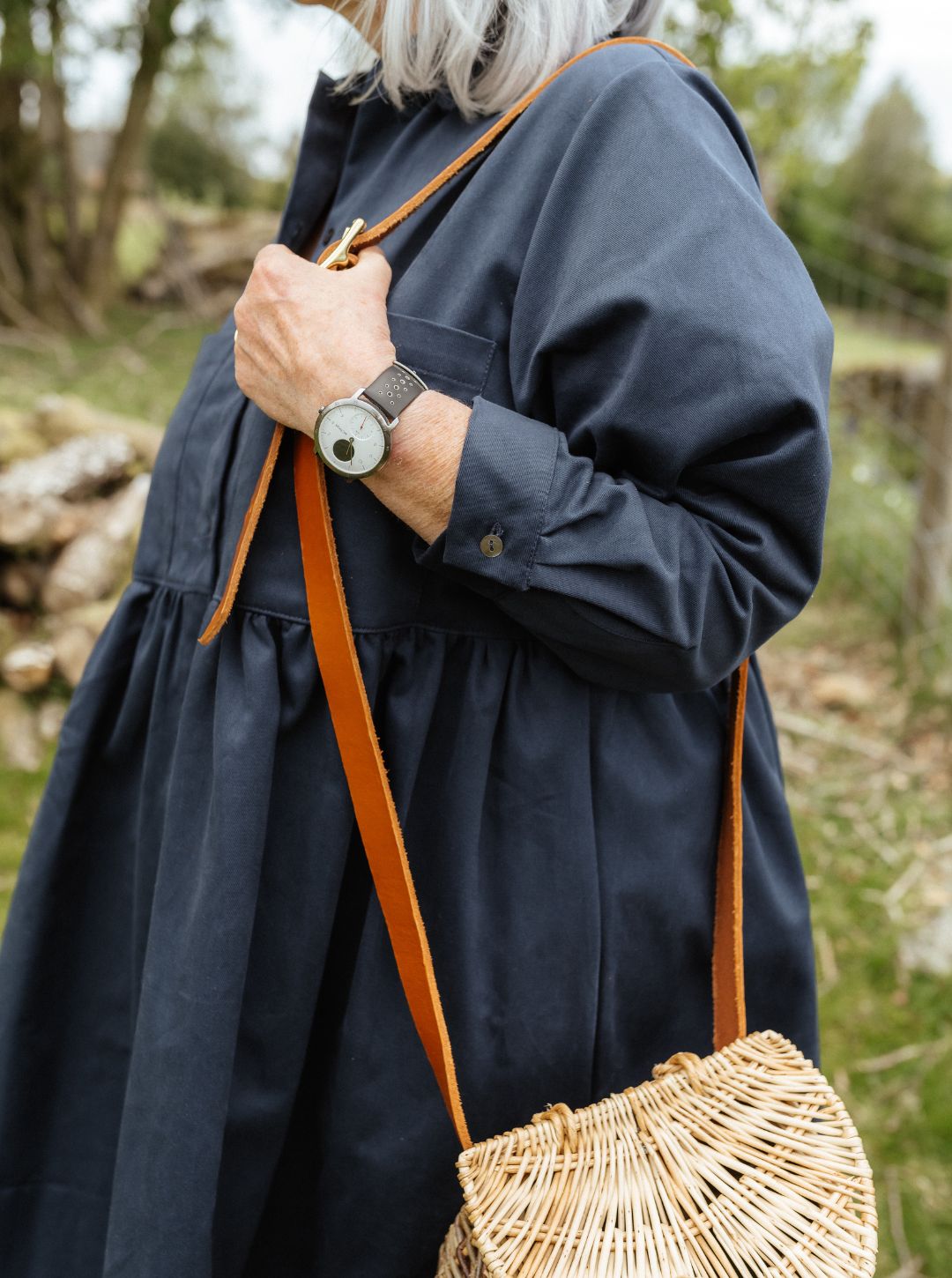 Person wearing a navy Dorothy shirtdress with a woven bag over their shoulder in a natural setting.