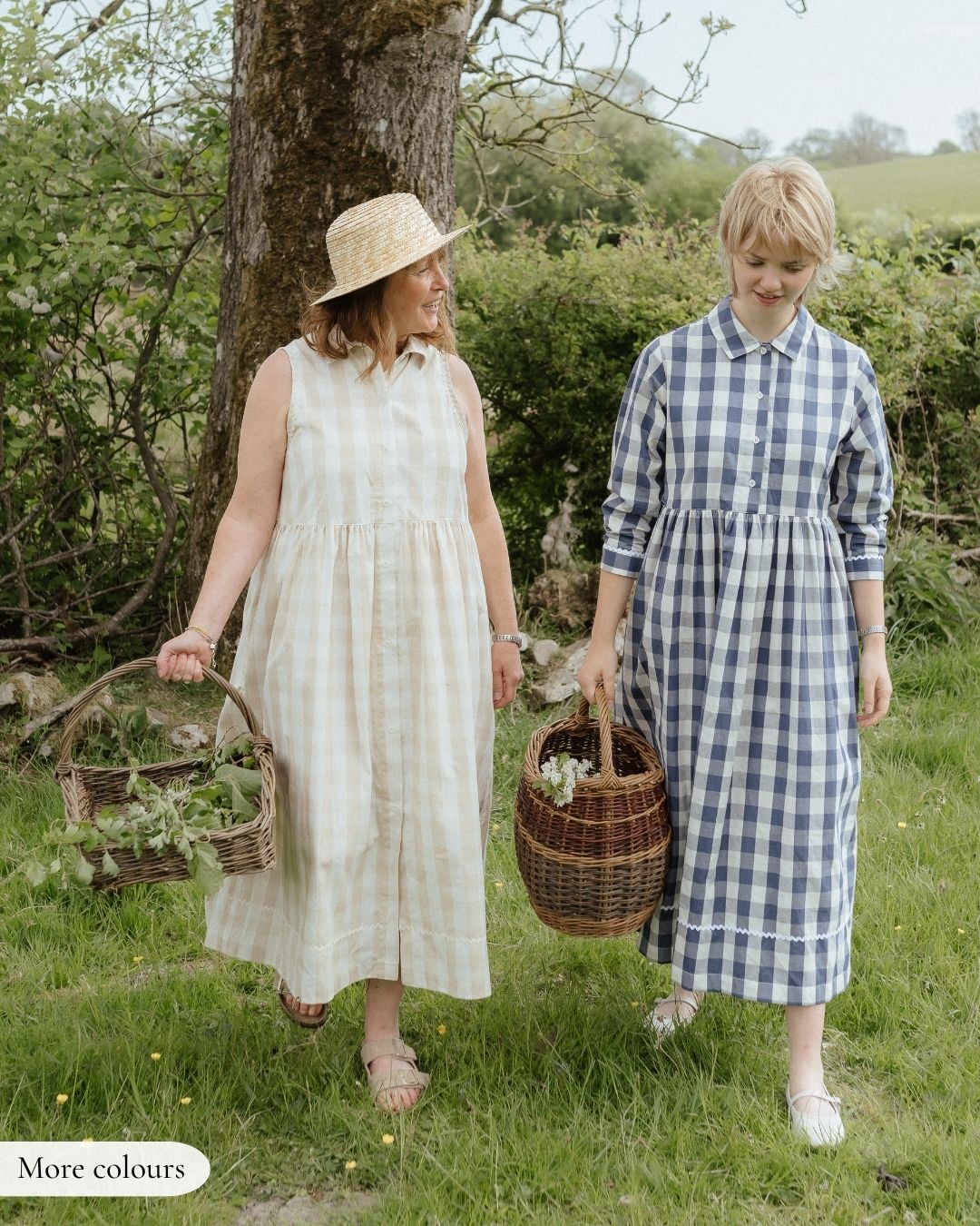 Two women in long dresses walking outdoors with baskets, surrounded by greenery.
