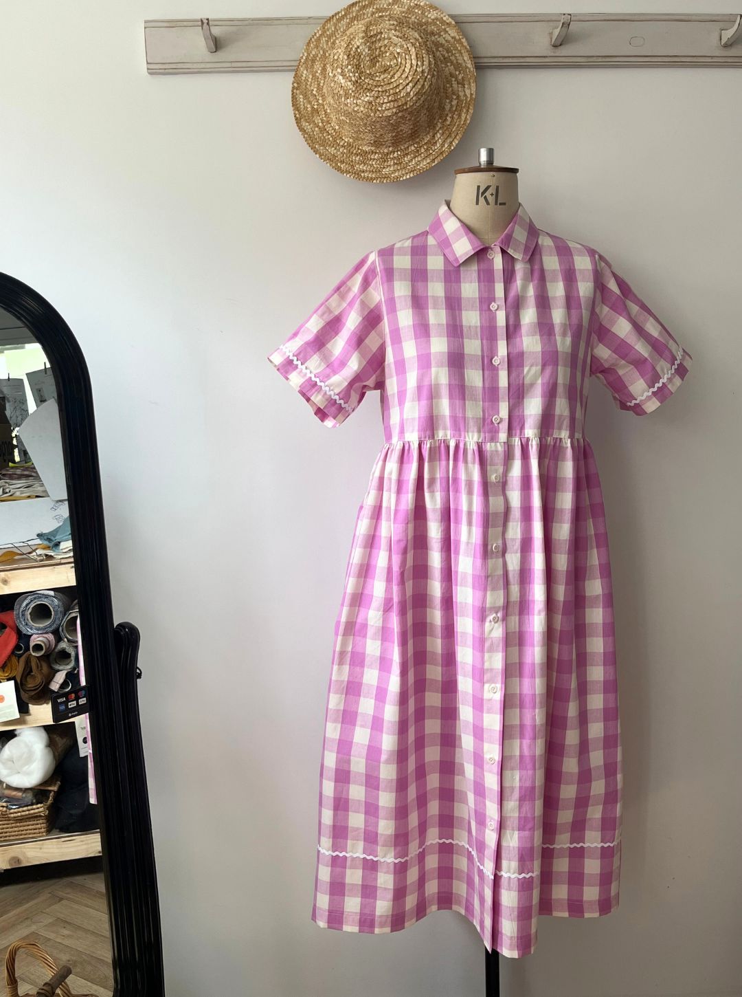 Pink and white checkered dress on a mannequin against a plain wall.