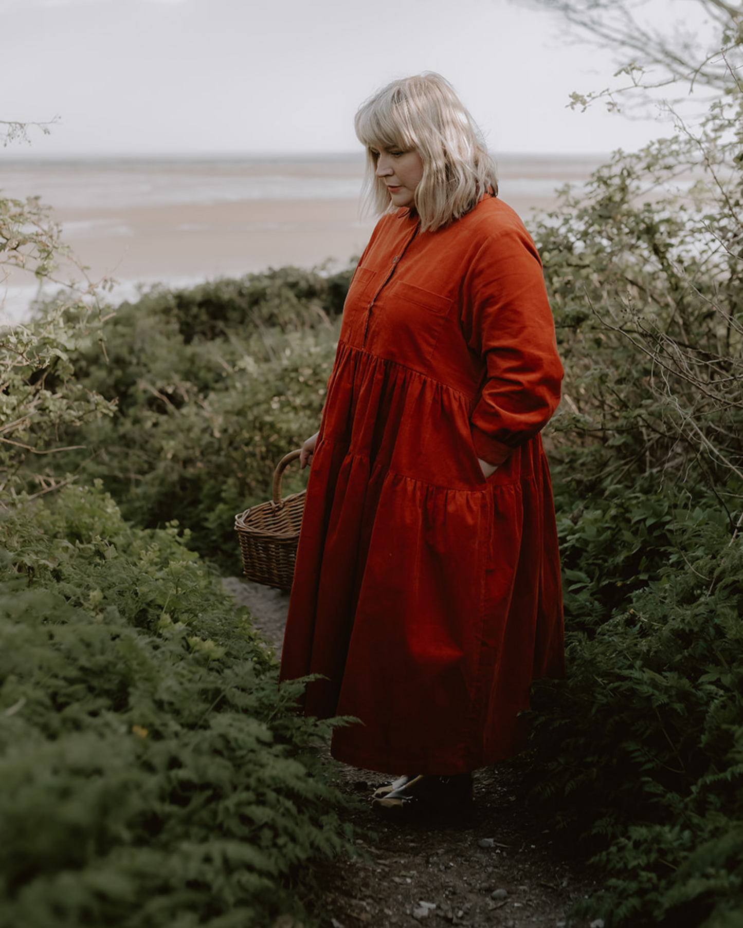 woman standing on path on coastal setting holding a basket.