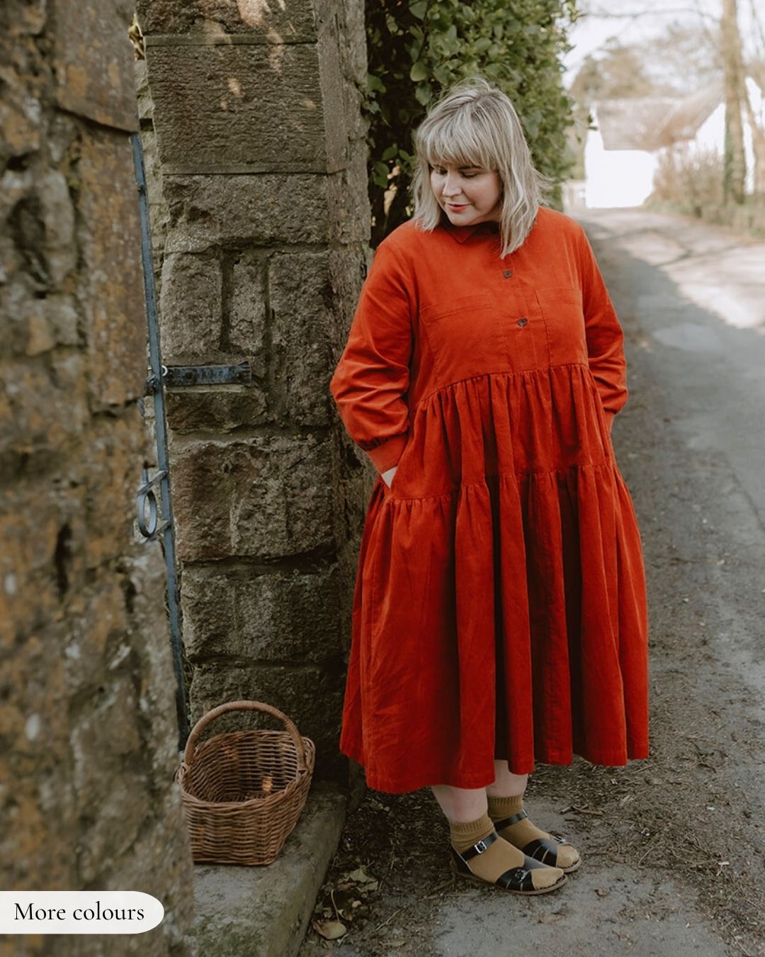 Woman in a red dress standing next to a stone wall with a wicker basket.