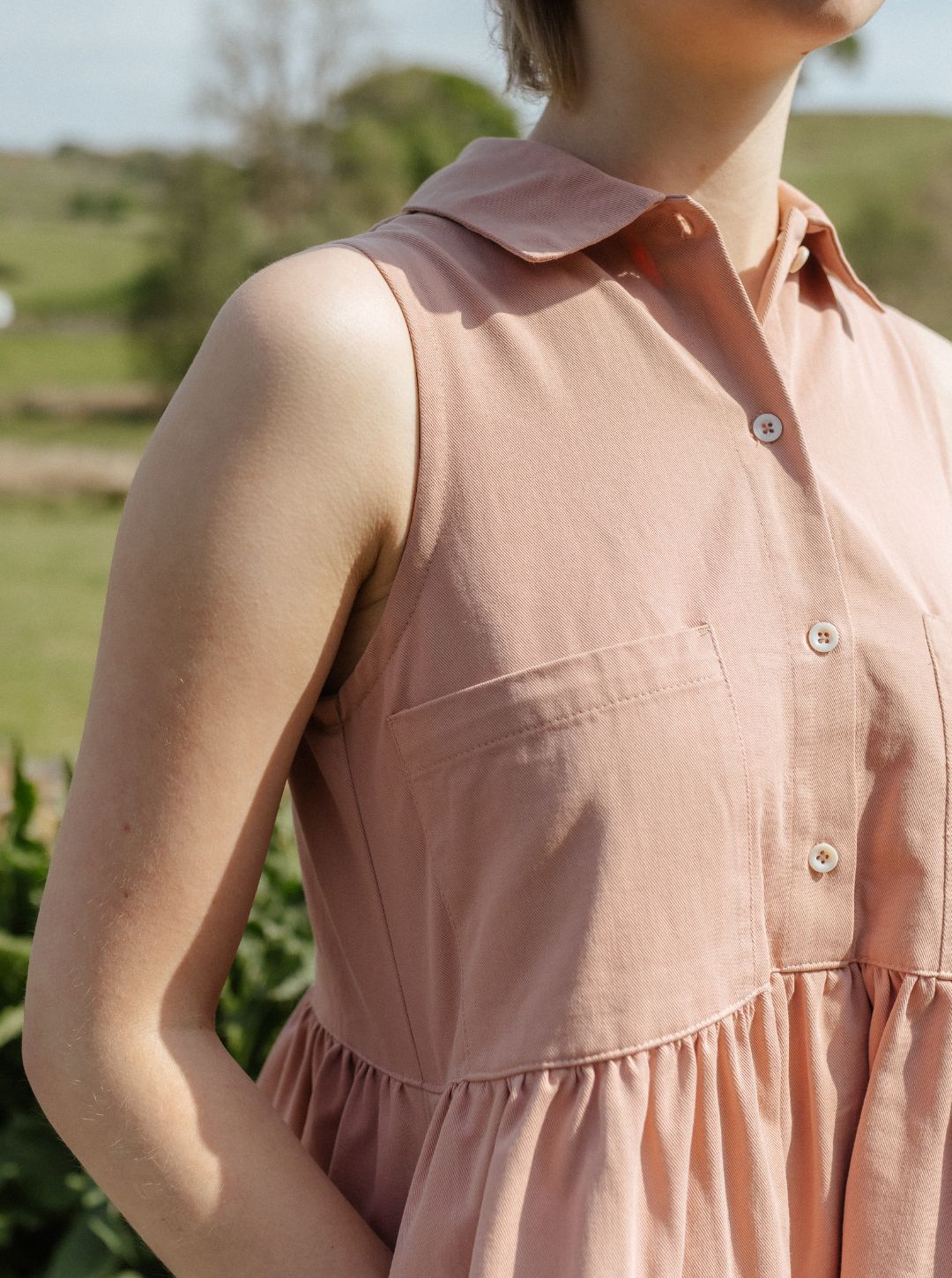 Person wearing a sleeveless pink dress with a blurred natural background