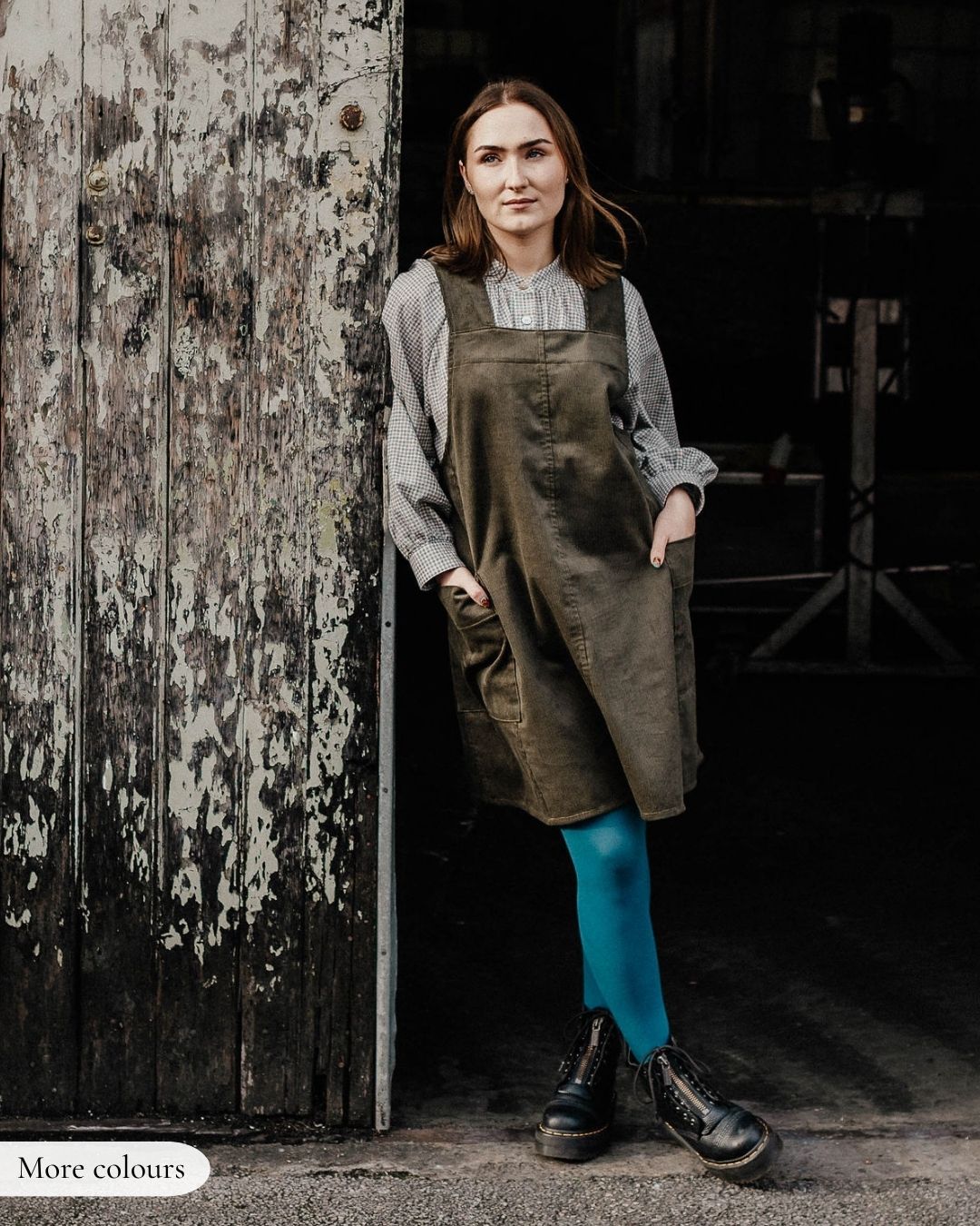 Woman wearing a brown apron standing in front of a rustic wooden door.