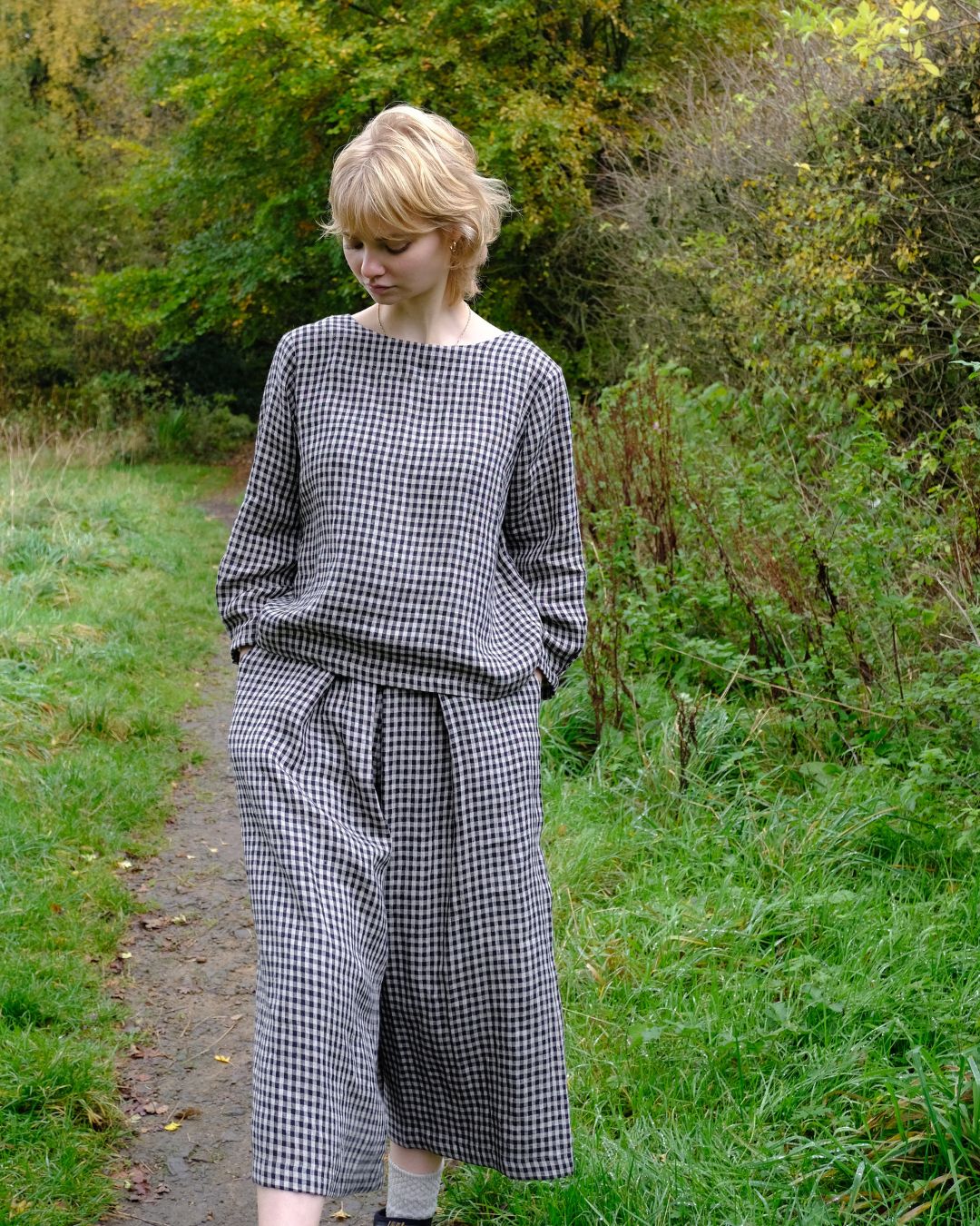 Woman wearing a black and white checkered outfit standing in a natural setting with greenery.