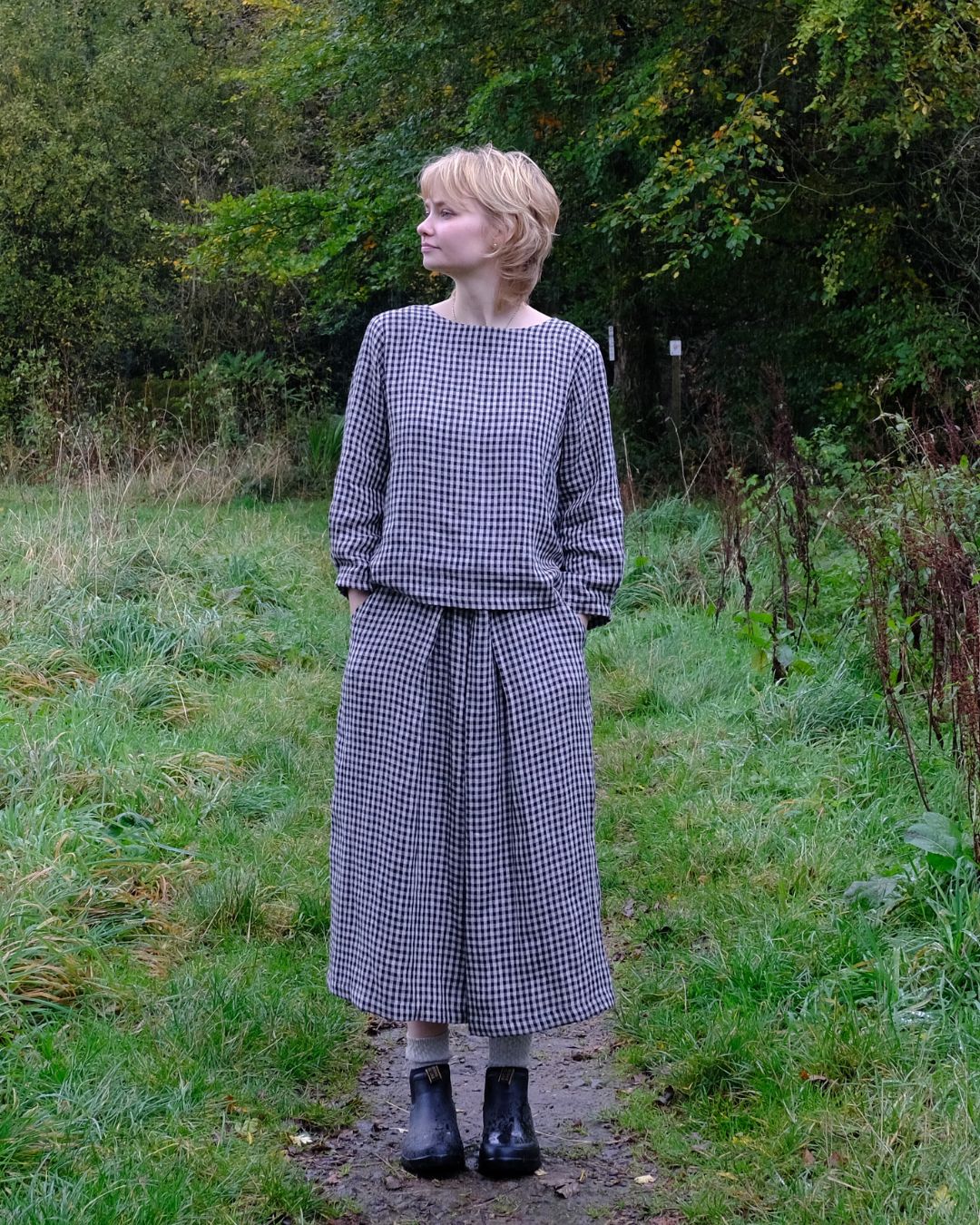 Woman wearing a checkered outfit standing in a natural setting with greenery.