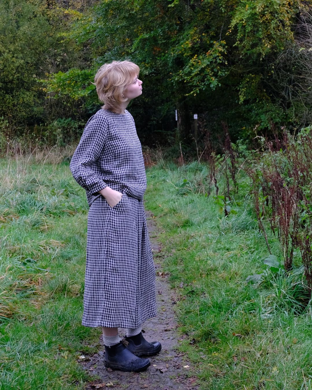 Person wearing a checkered dress standing on a path in a natural setting