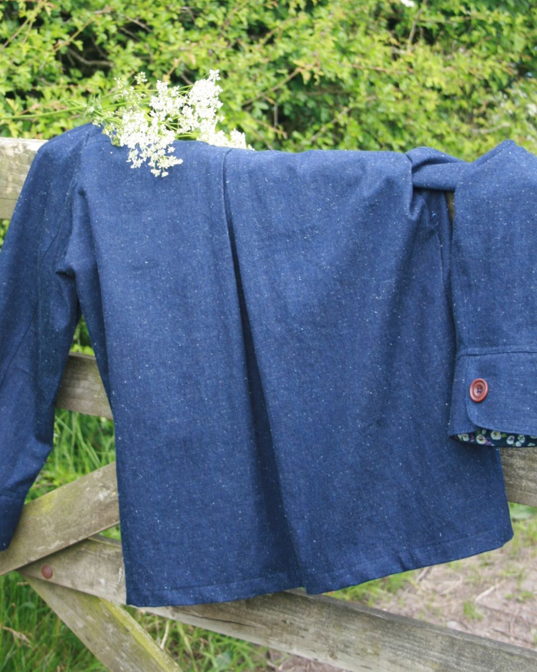 Blue jacket draped over a wooden fence with greenery in the background