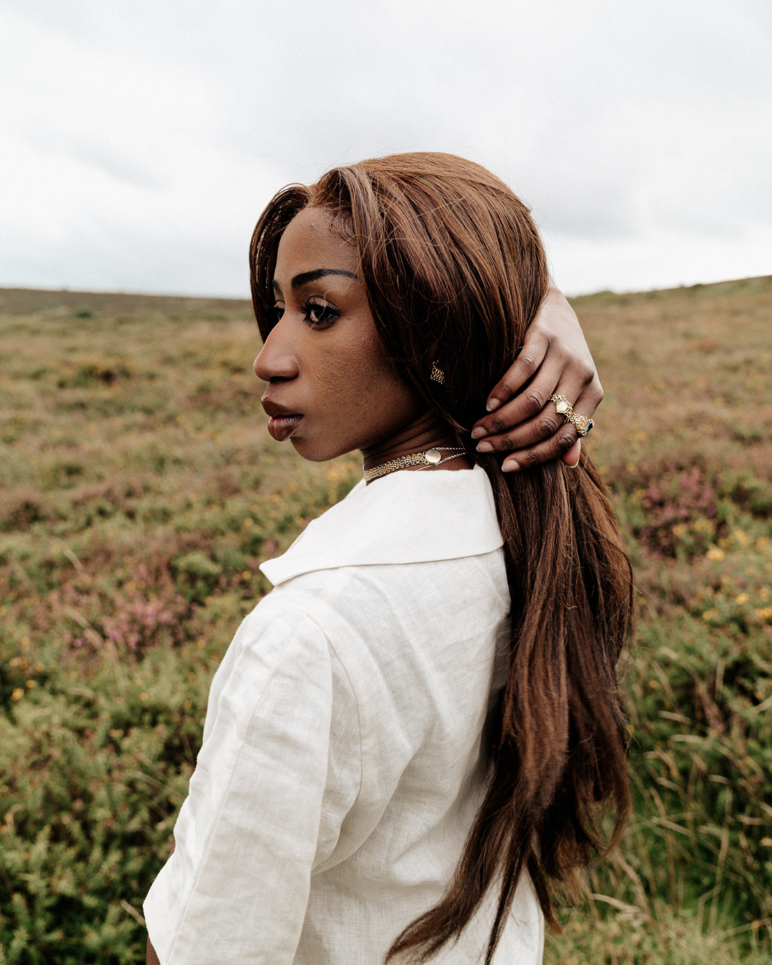 Woman wearing a cream linen blouse standing holding hair in a moorland setting