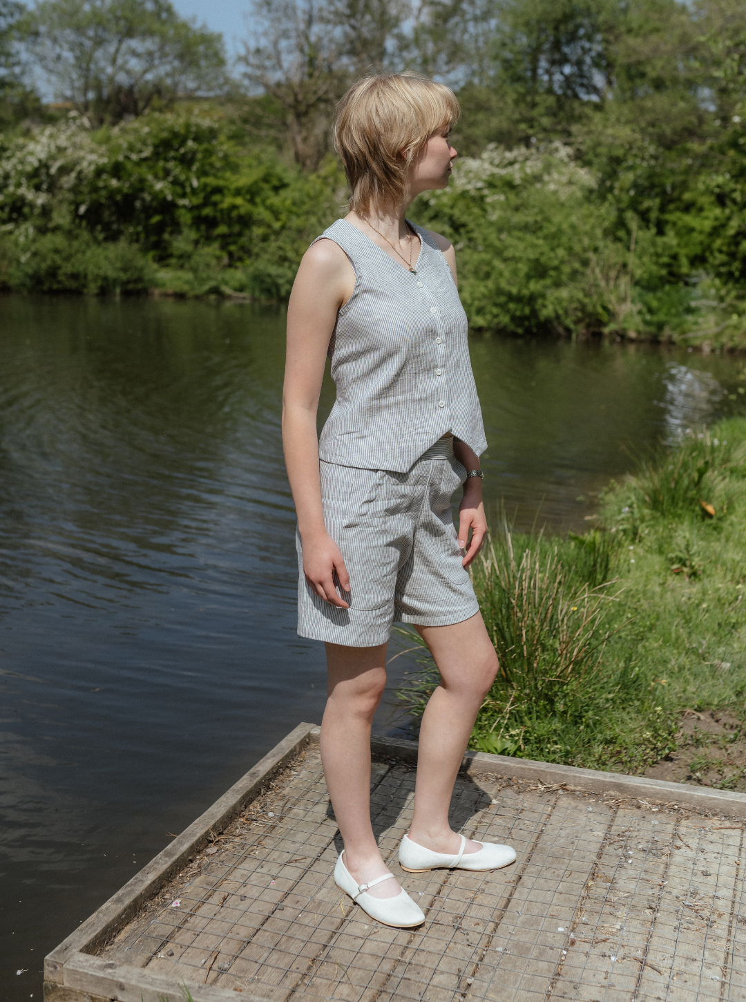 Woman in a light gray sleeveless top and shorts standing on a wooden platform by a body of water.