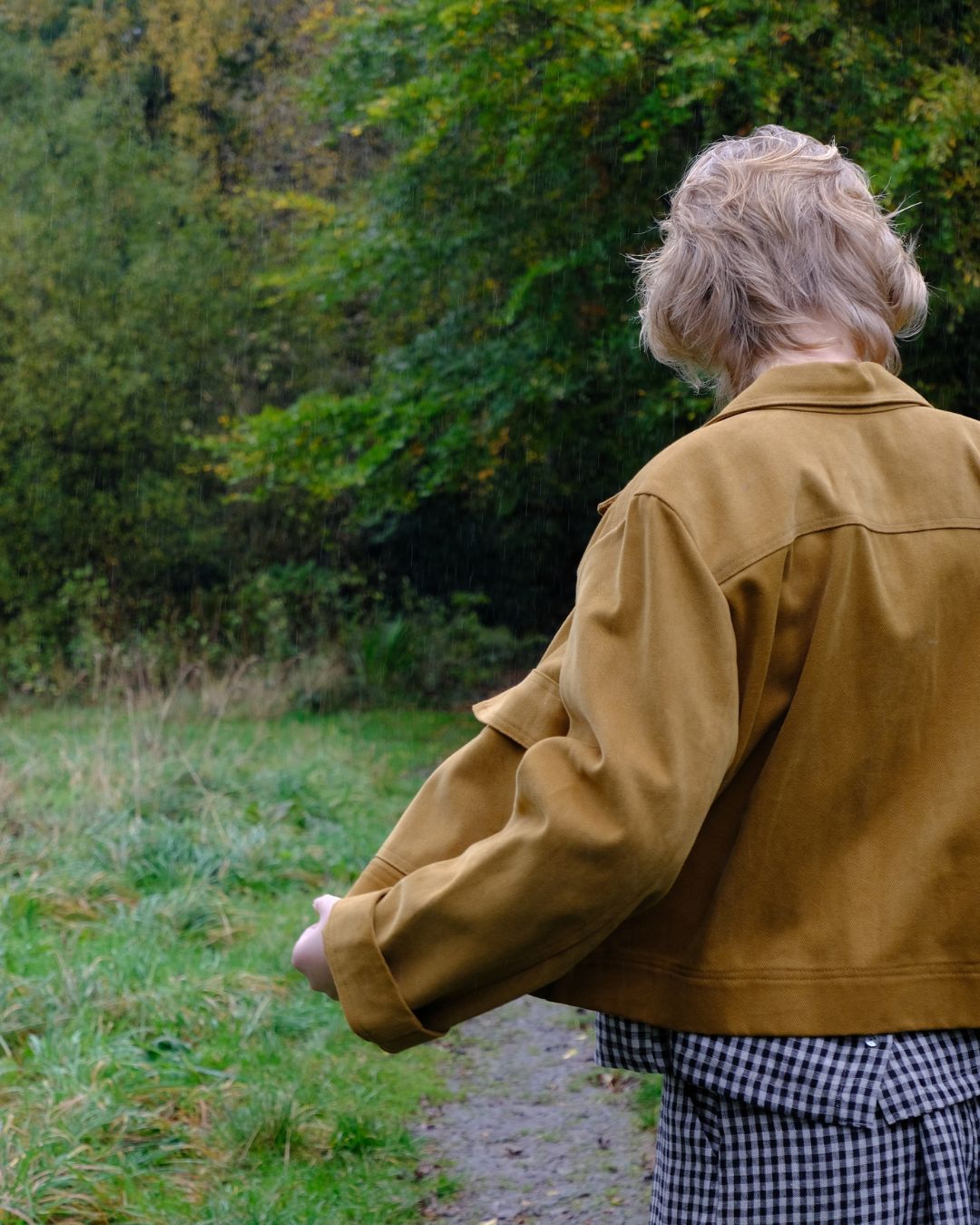 Person wearing a brown jacket walking on a path with greenery in the background