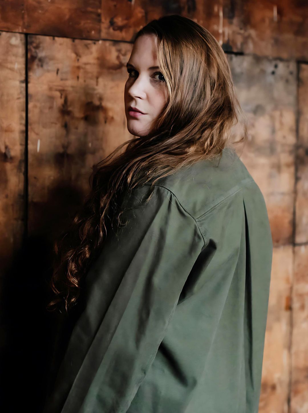 Woman wearing a green jacket - showing back pleat against a wooden wall