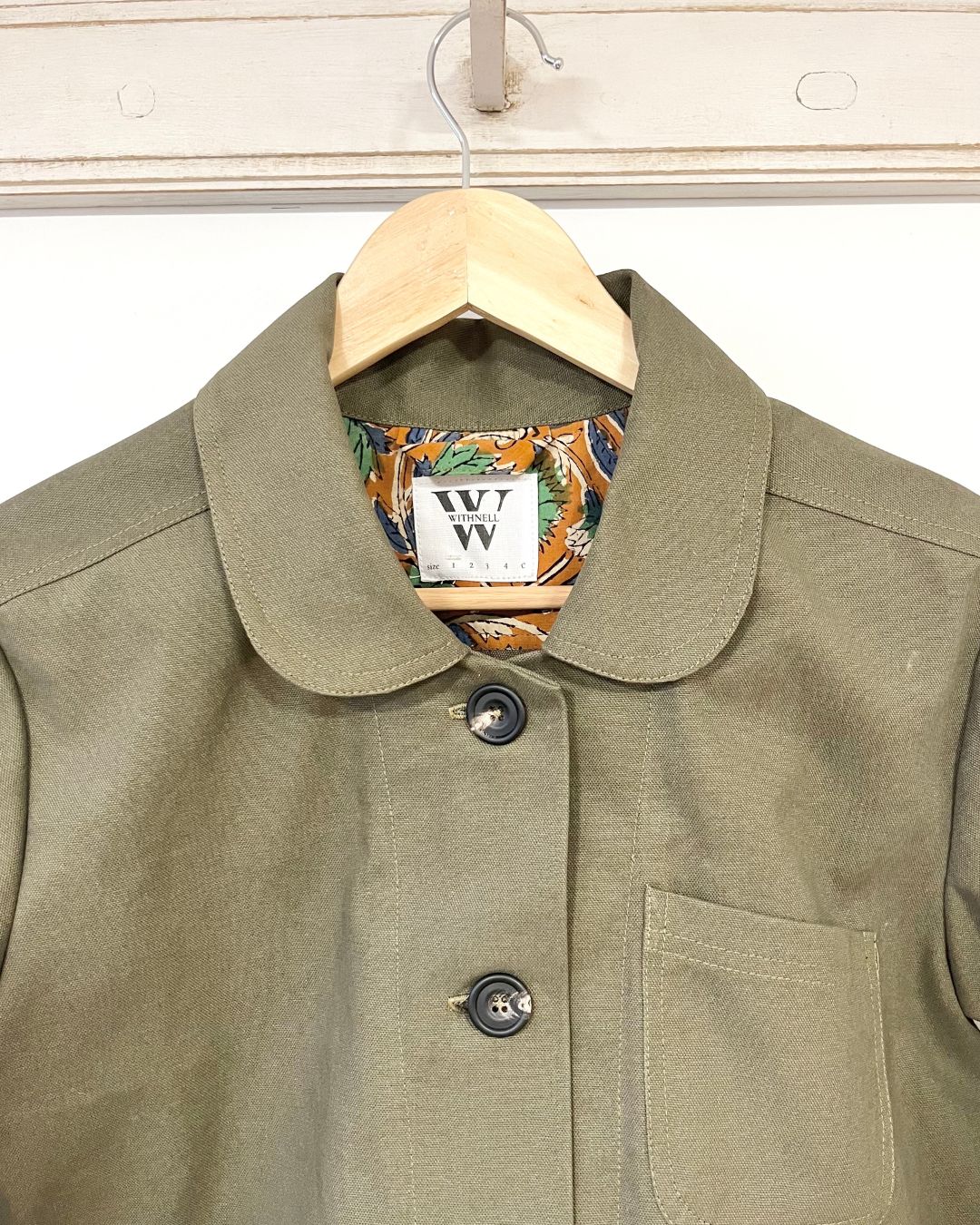 Green jacket showing a patterned collar on a hanger against a white background
