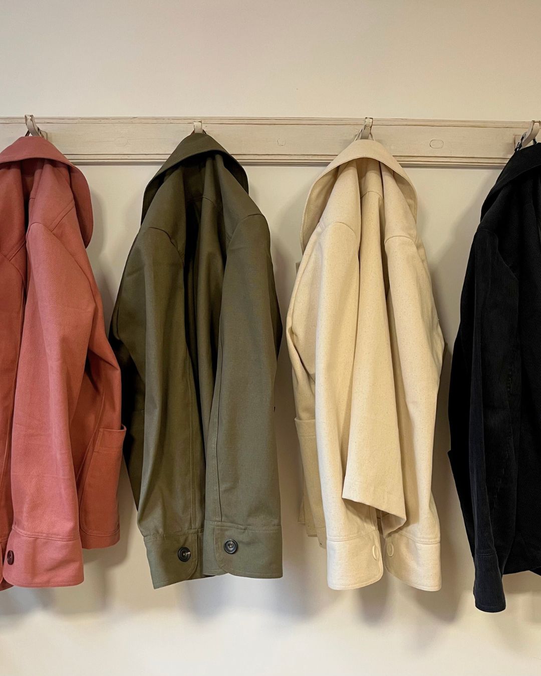 Four jackets hanging on a rack against a white wall -all different fabric options for the jacket.