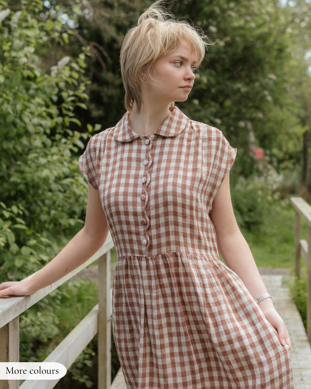 Woman wearing a checkered dress standing outdoors with greenery in the background