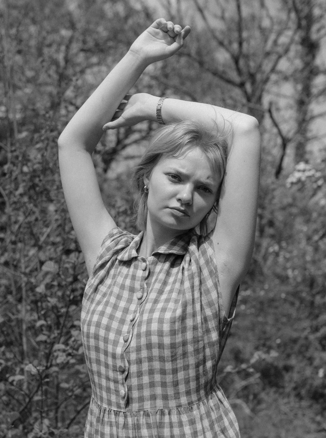 Black and white photo of a woman in a checkered dress posing outdoors.