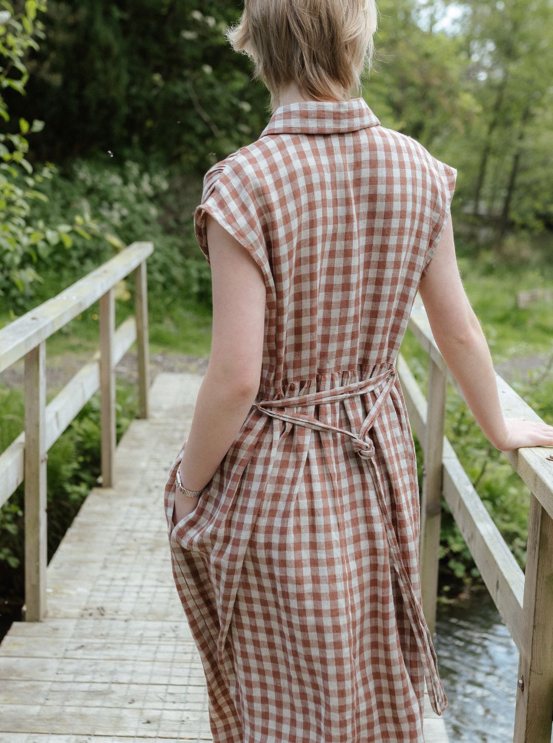 Woman in a checkered dress standing on a wooden bridge in a natural setting
