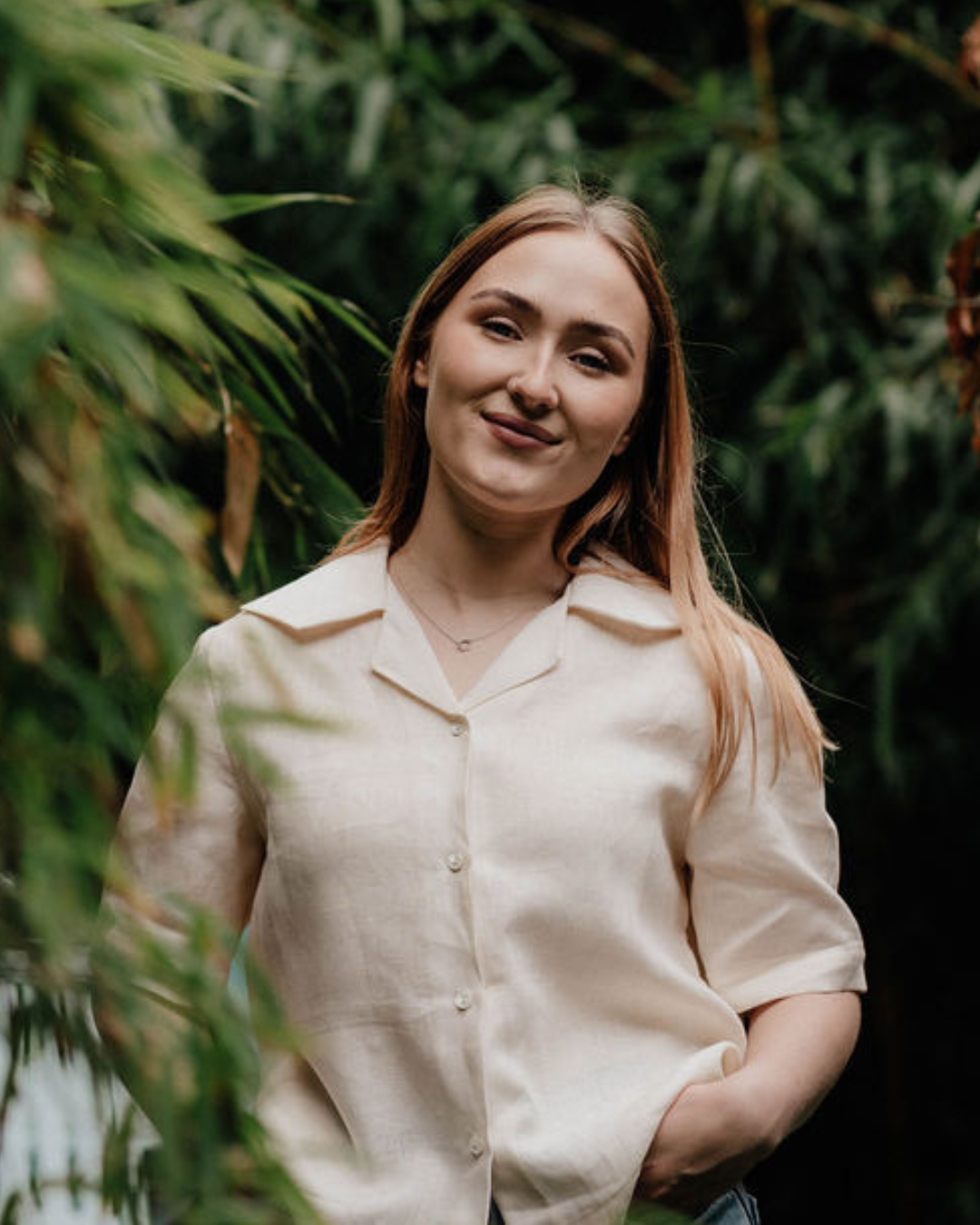 Woman wearing a cream linen blouse standing holding hair in a moorland setting