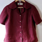 Maroon shirt on a hanger against a white wall