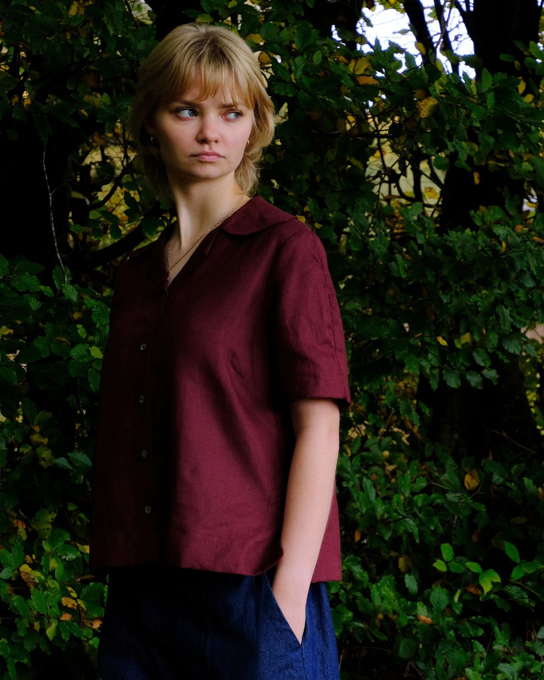 person wearing damson top with greenery inn background