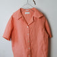 Coral-colored shirt on a hanger against a plain background