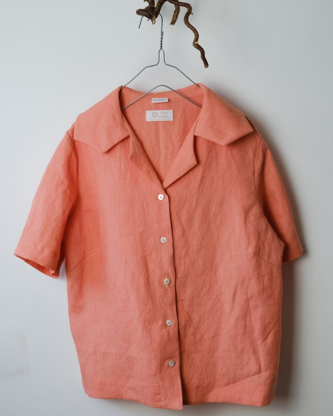 Coral-colored shirt on a hanger against a plain background