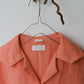 Coral shirt on a hanger with a visible brand label against a neutral background