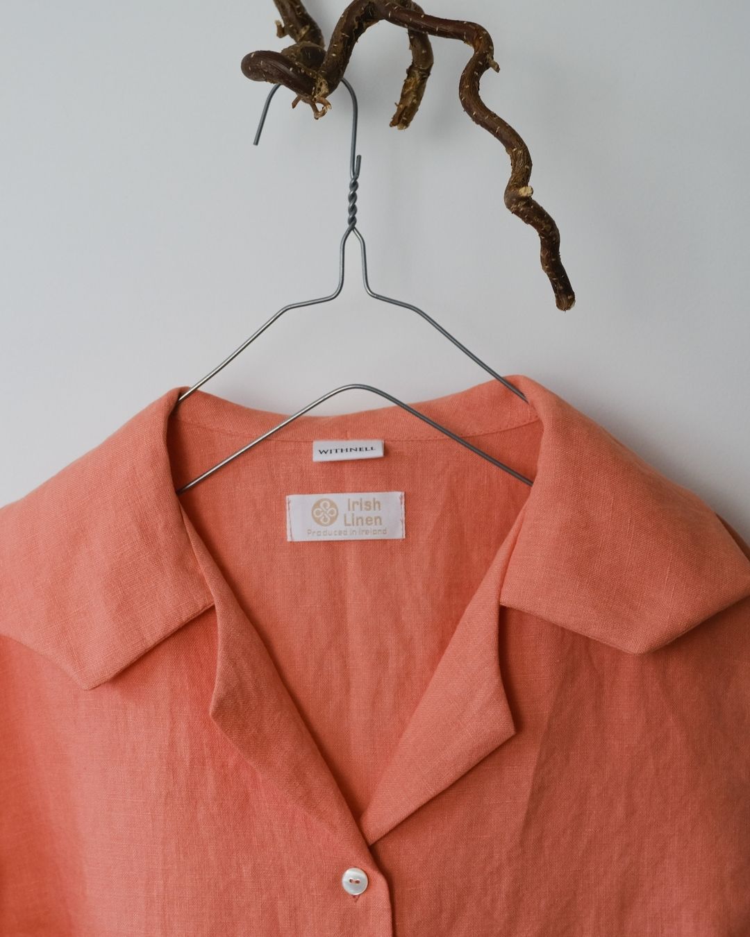 Coral shirt on a hanger with a visible brand label against a neutral background