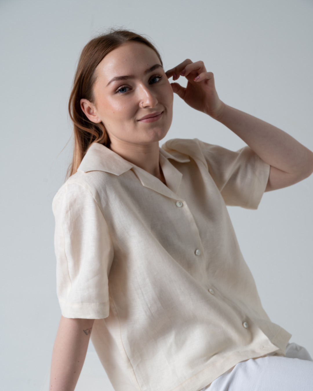 Woman wearing a cream linen blouse  sitting down in studio