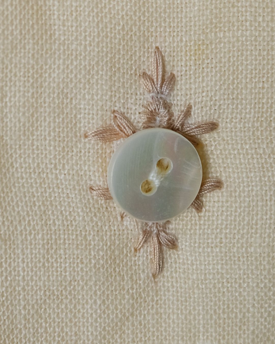 Button with decorative leaves on a beige fabric background