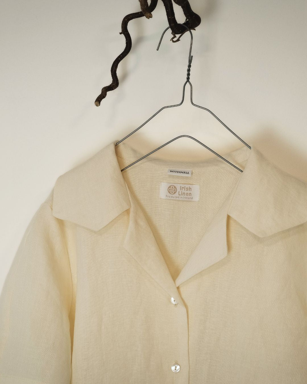 ivory shirt on a hanger with a visible label against a plain background