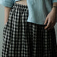 A close-up of a person wearing a black and white gingham check skirt with an elastic waistband, styled with a light blue cropped linen shirt.