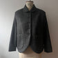 A dark gray textured wool jacket with a Peter Pan collar and front buttons, displayed on a vintage mannequin torso against a plain light gray wall.