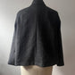 A dark gray textured wool cape jacket displayed on a cream-colored dress form mannequin, showing the back view against a neutral gray background.