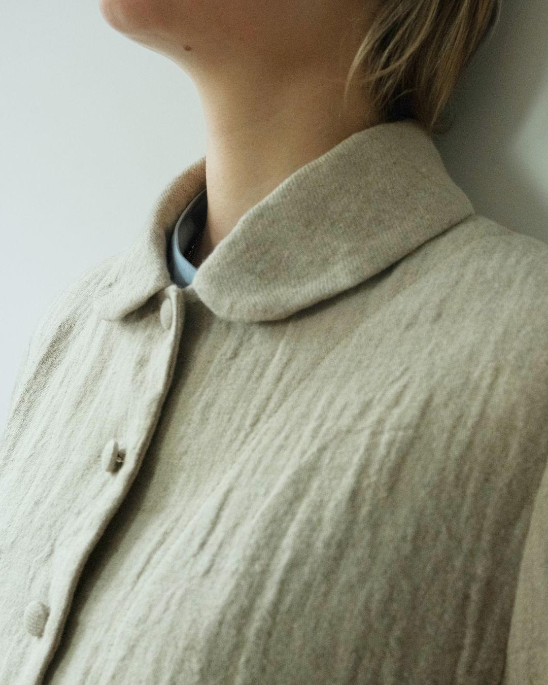 Close-up of a person wearing a textured linen jacket from Withnell with a collar and front buttons, layered over a light blue shirt.