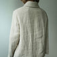 A person viewed from the back wearing a light beige linen-textured collared jacket or shirt against a plain light gray wall.