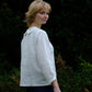 Woman wearing a white shirt standing against a dark green leafy background