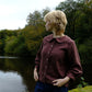 Person wearing a maroon shirt standing by a body of water with trees in the background