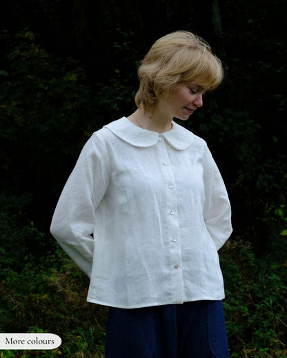 Woman wearing a white blouse with a Peter Pan collar against a dark background