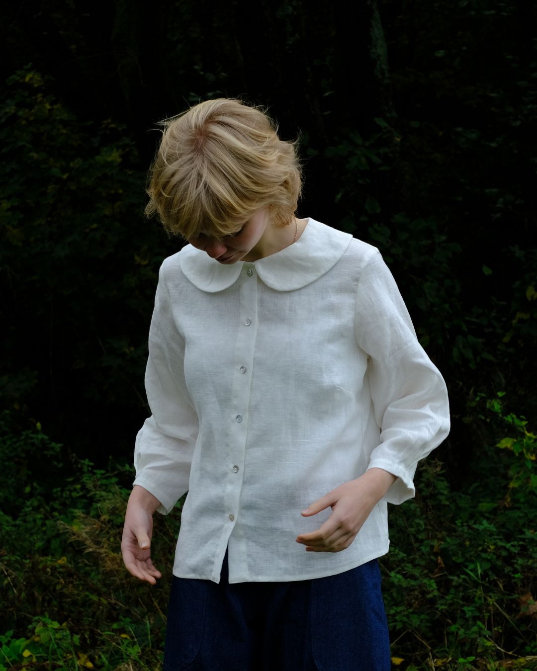 Person wearing a white blouse with a Peter Pan collar in a natural setting.