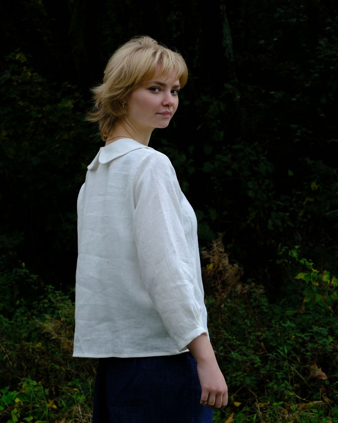 Woman wearing a white shirt standing against a dark green leafy background