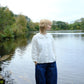 Person standing by a lake wearing a white blouse and blue pants