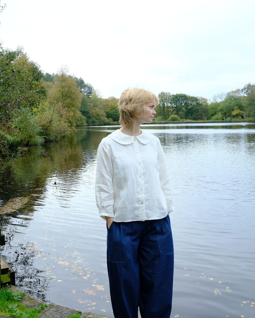 Person standing by a lake wearing a white blouse and blue pants